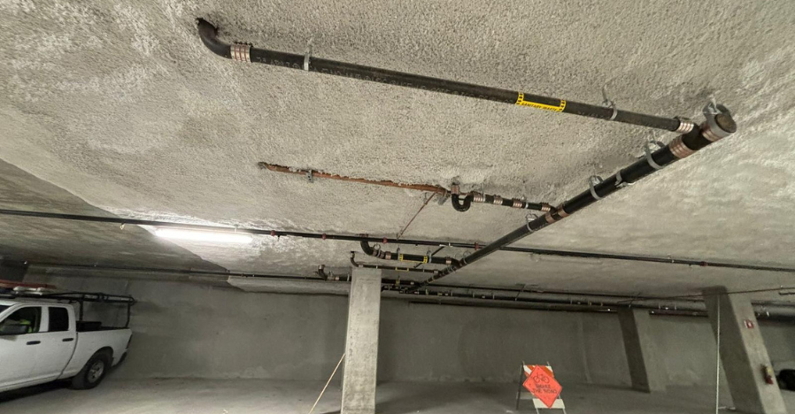 Image of a basement ceiling with several insulated pipes installed, a white pickup truck, and an orange construction sign in Martinez, showcasing the work of Insul-Techs Inc.